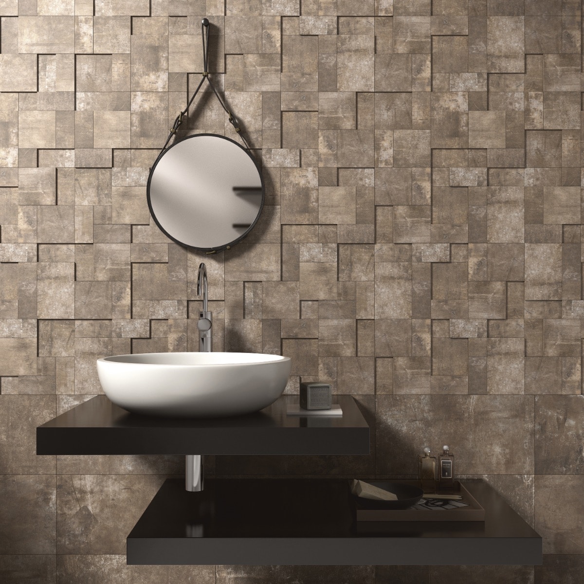 Een badkamer met een mozaïekmuur van tegels in een verweerde, grijze kleur met een geometrisch, textuurpatroon en een ronde spiegel boven een minimalistische wastafel.